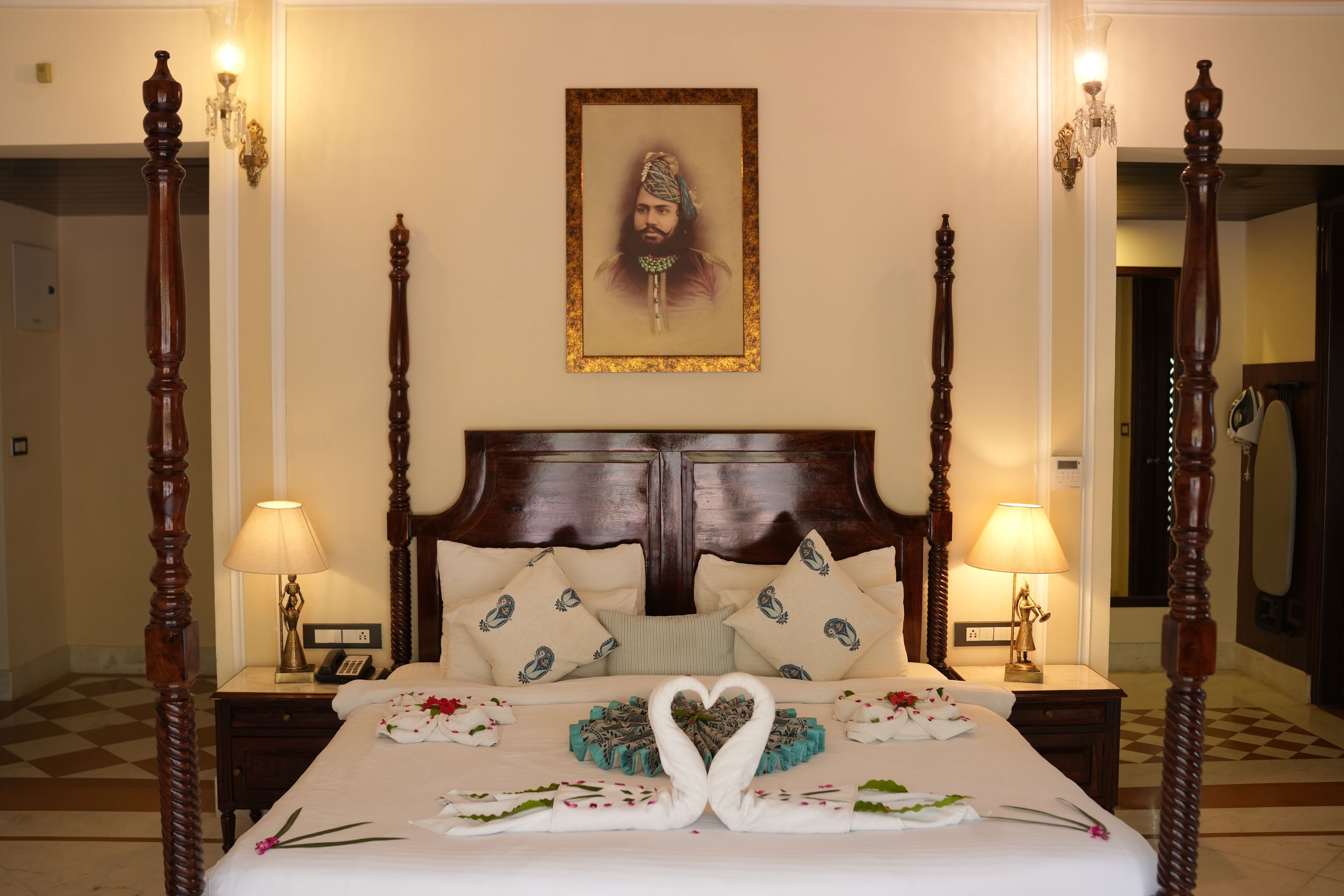 Uma cama com dossel e cabeceira de madeira, duas luminárias de apoio e um retrato emoldurado acima.