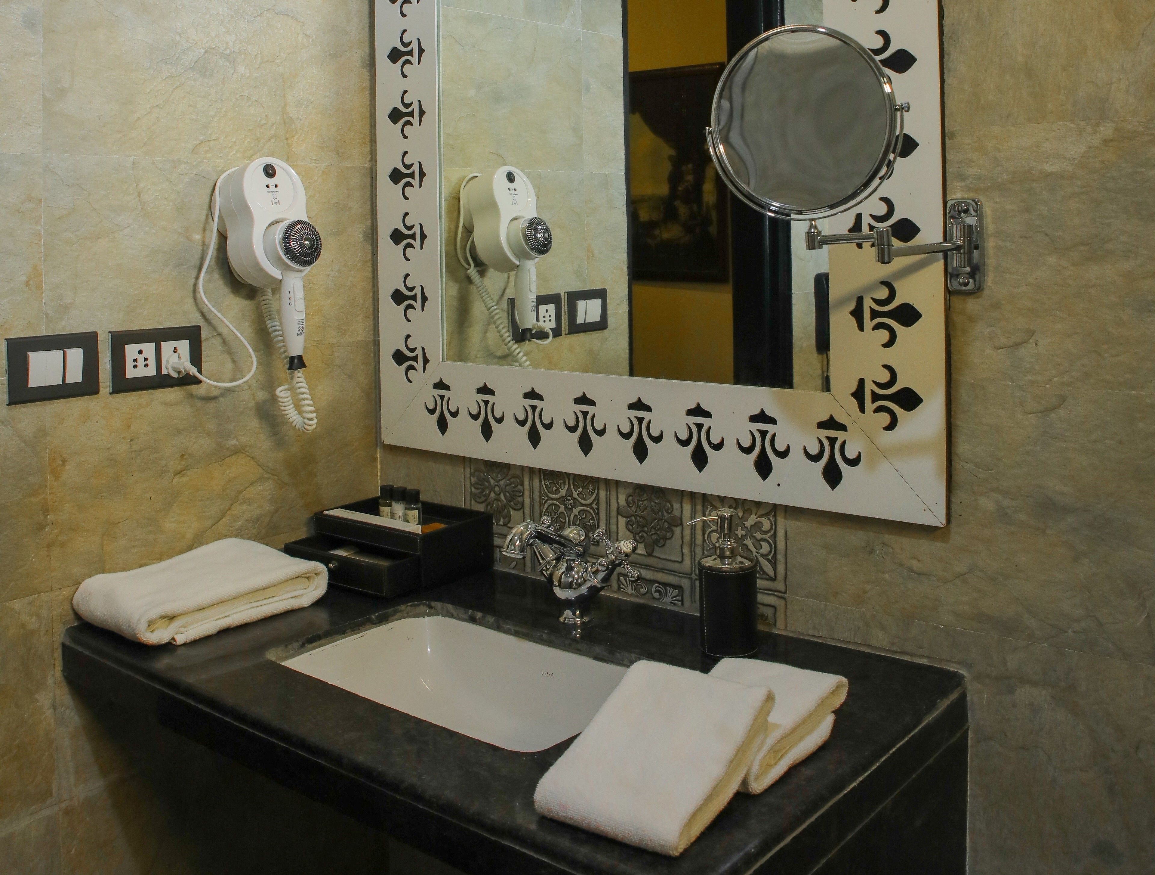 A bathroom with a black countertop, a white sink, two towels, a mirror, a hairdryer, and a wall-mounted phone.