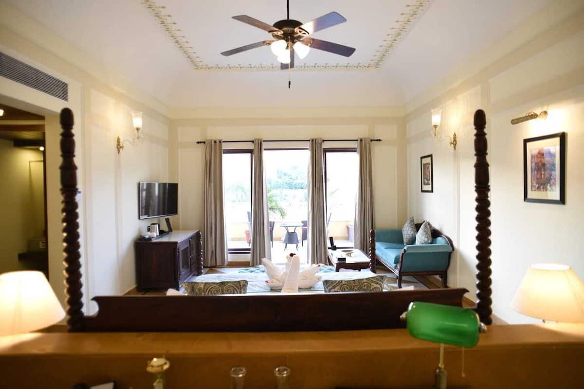 Et hotelværelse med seng, fjernsyn, sofa og en balkon med gardiner.