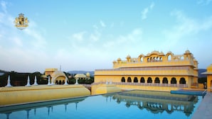 Un edificio grande y amarillo con ventanas de arco y cúpulas, reflejado en una piscina.