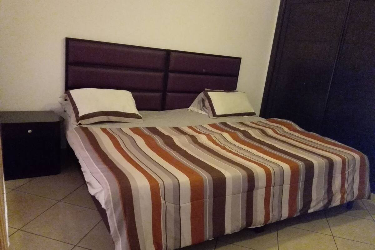 Una cama con colcha a rayas, cabecero y dos almohadas.