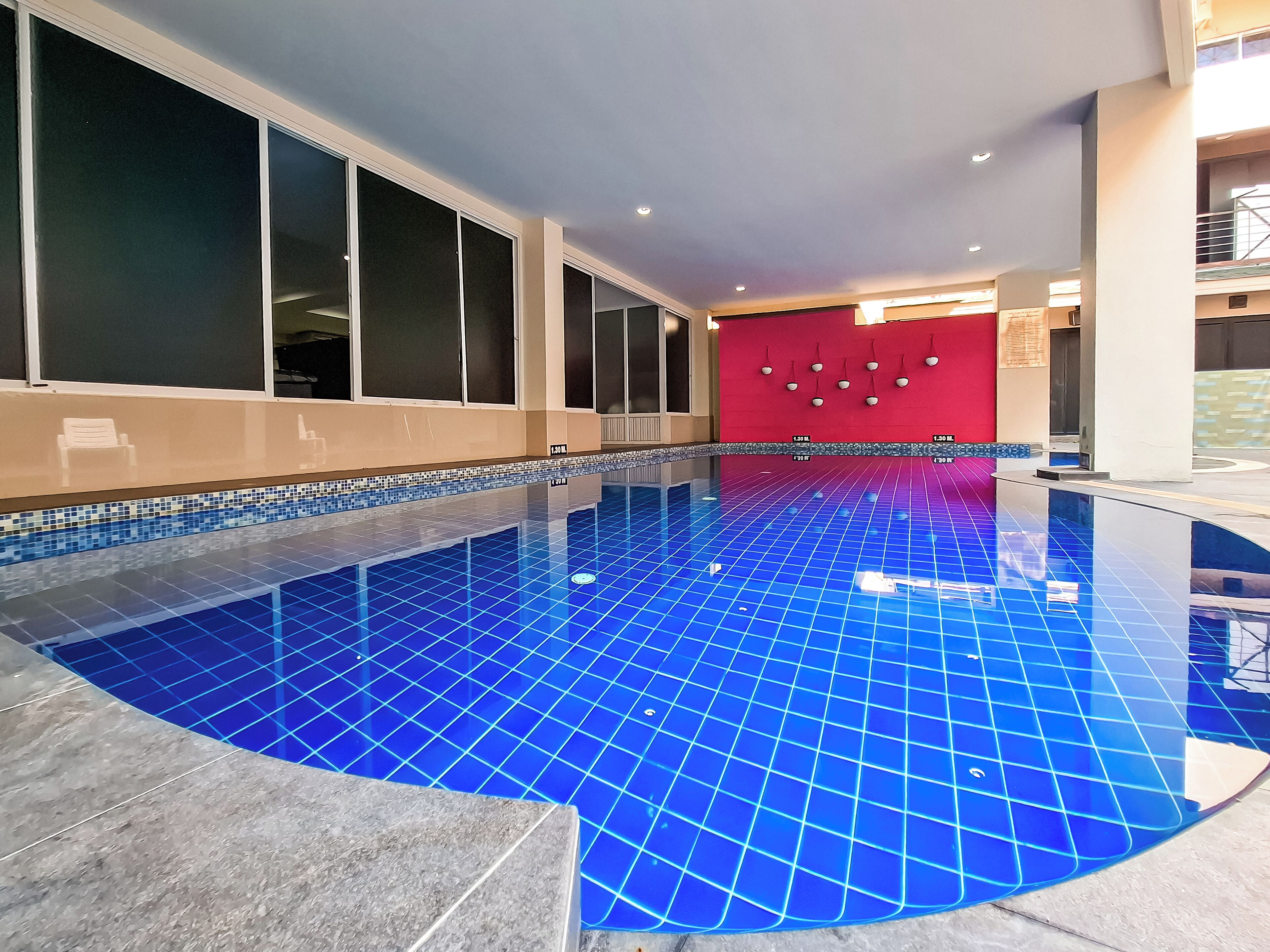 An indoor swimming pool with blue tiled flooring and a red wall in the background.