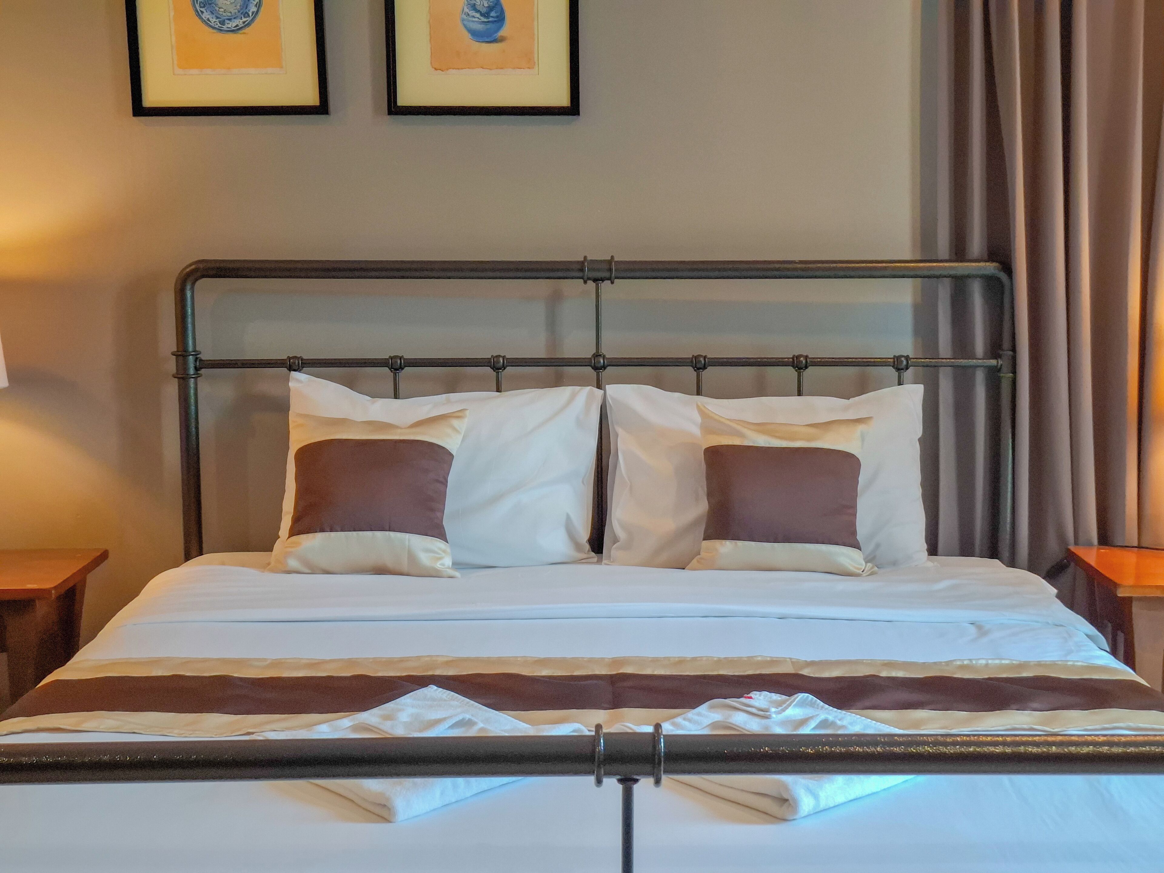 Una cama bien tendida con un cabecero de metal, dos almohadas y una manta.