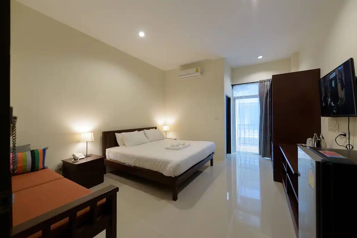 A hotel room with a bed, bedside lamps, a desk, a television, and a door leading to a balcony.