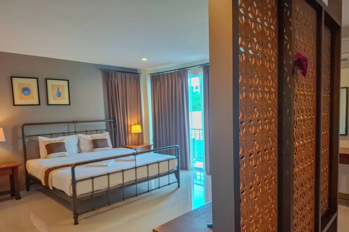 A hotel room with a double bed, a nightstand, a lamp, and a decorative screen.