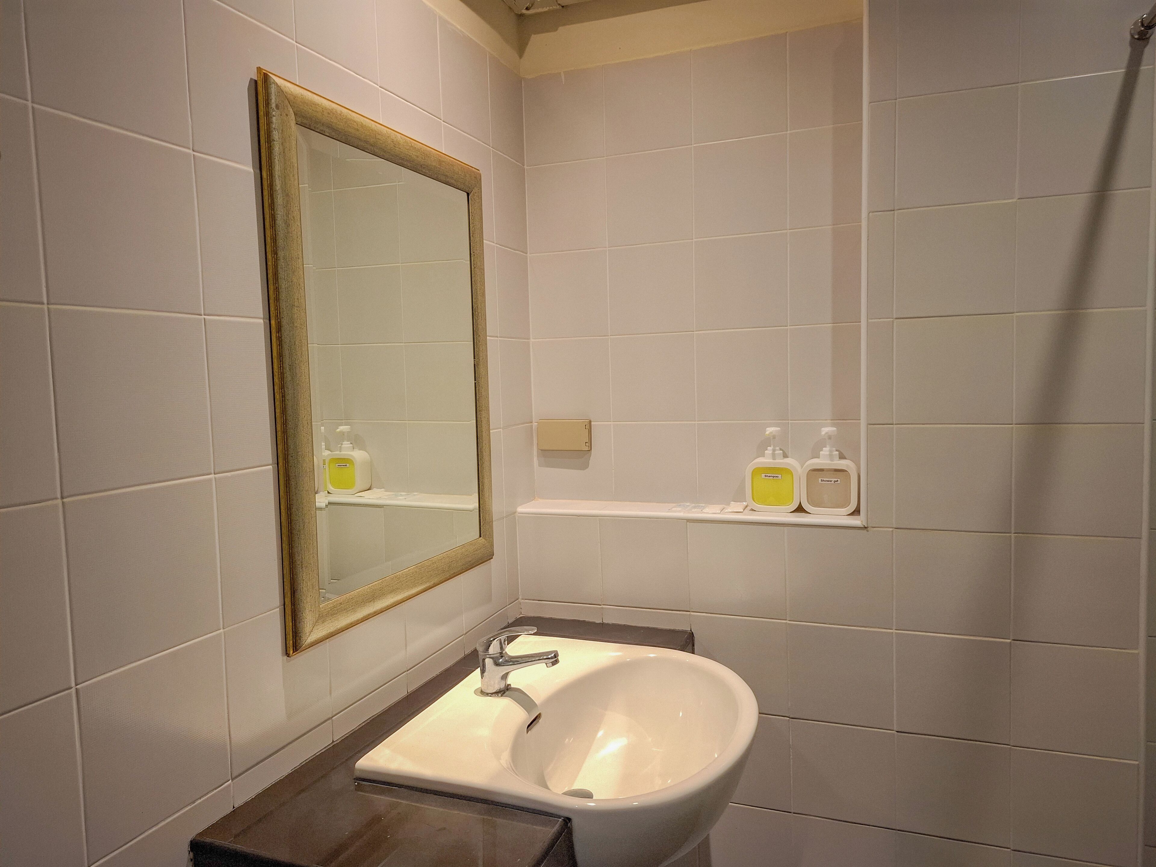 Ein Badezimmer mit einem weißen Waschbecken, einem Spiegel mit Holzrahmen und zwei Seifenflaschen auf einem Regal.