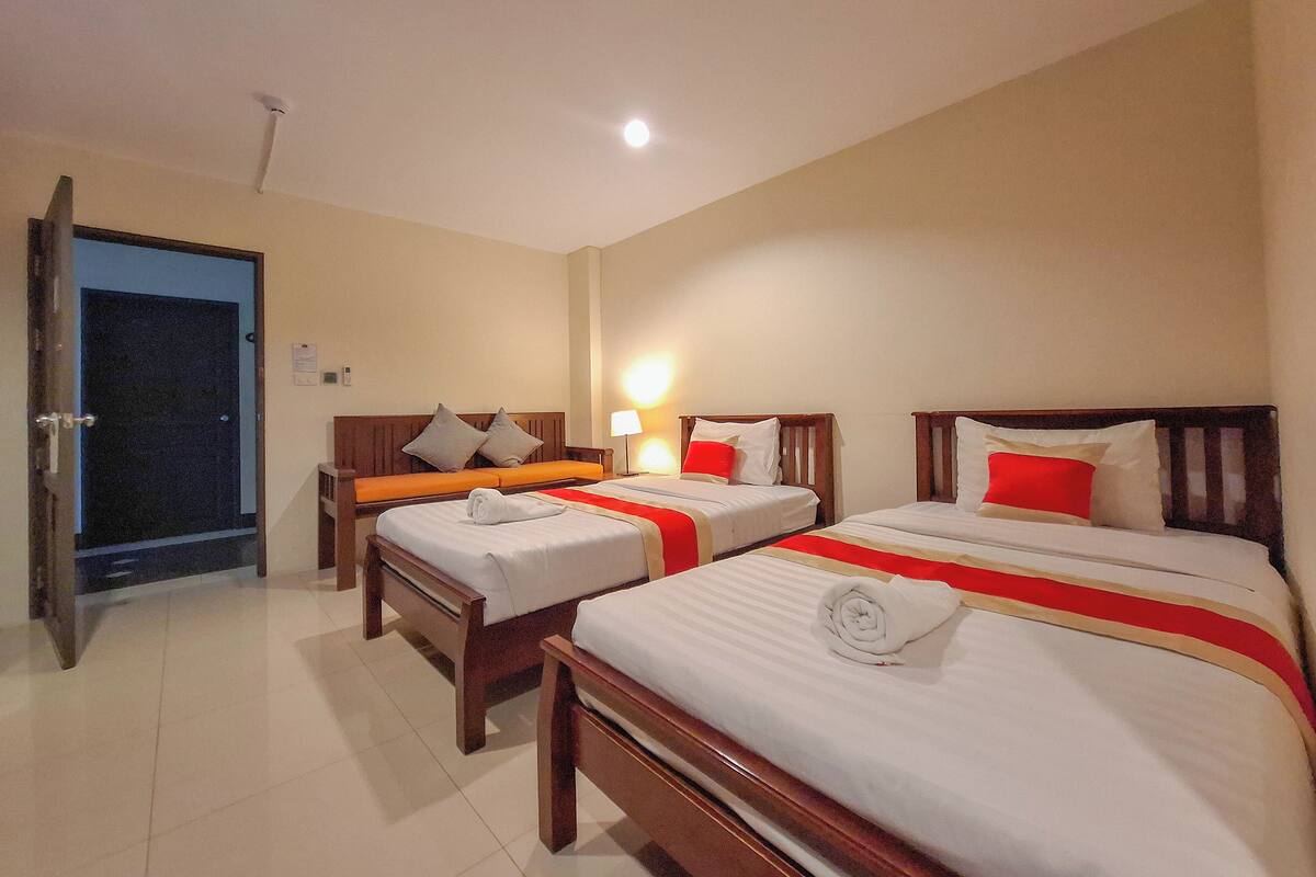 A hotel room with two beds, a door, and a nightstand with a lamp.