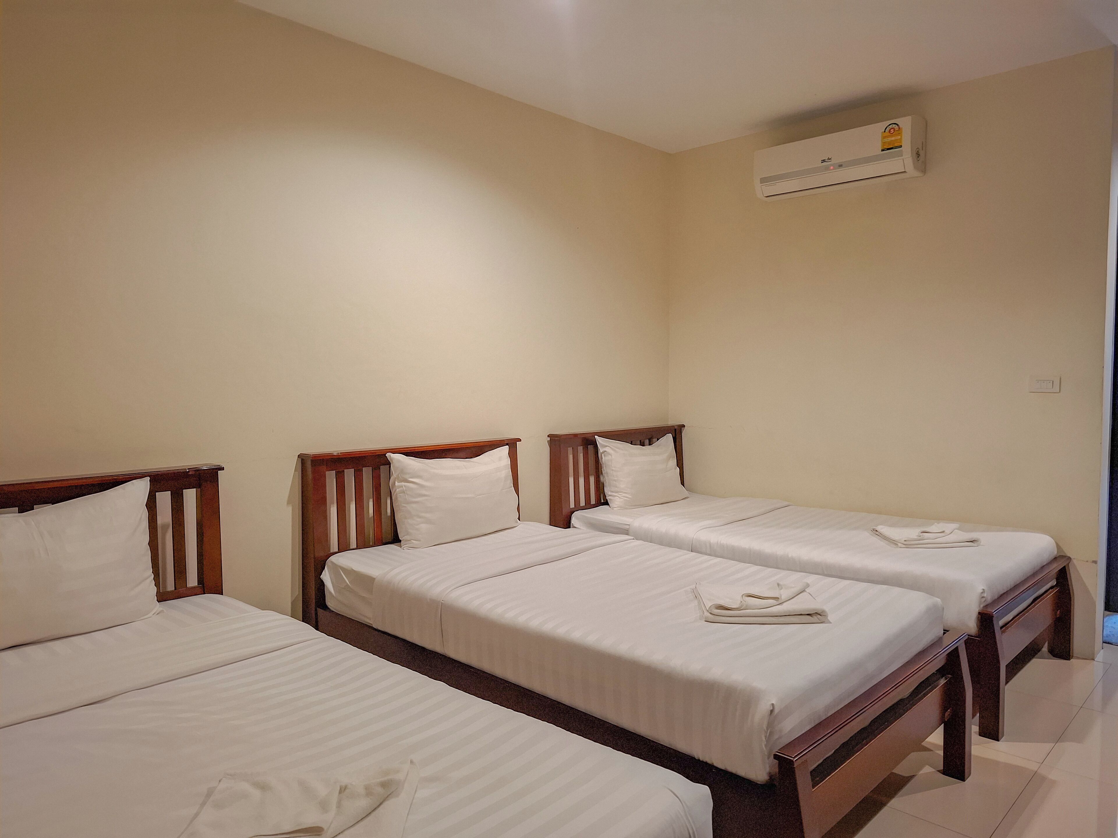 Ein Hotelzimmer mit drei Einzelbetten, alle mit Holz Kopfteilen und weißer Bettwäsche.