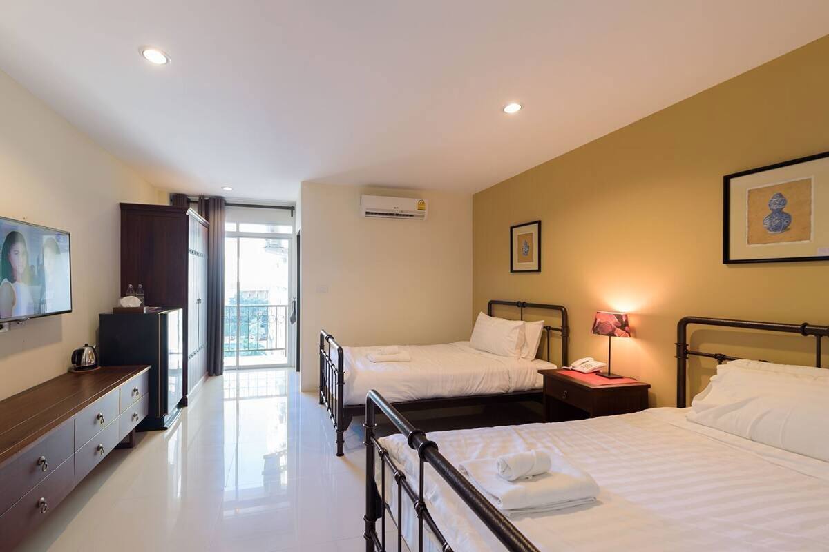A hotel room with two beds, a TV, a desk, and a balcony.