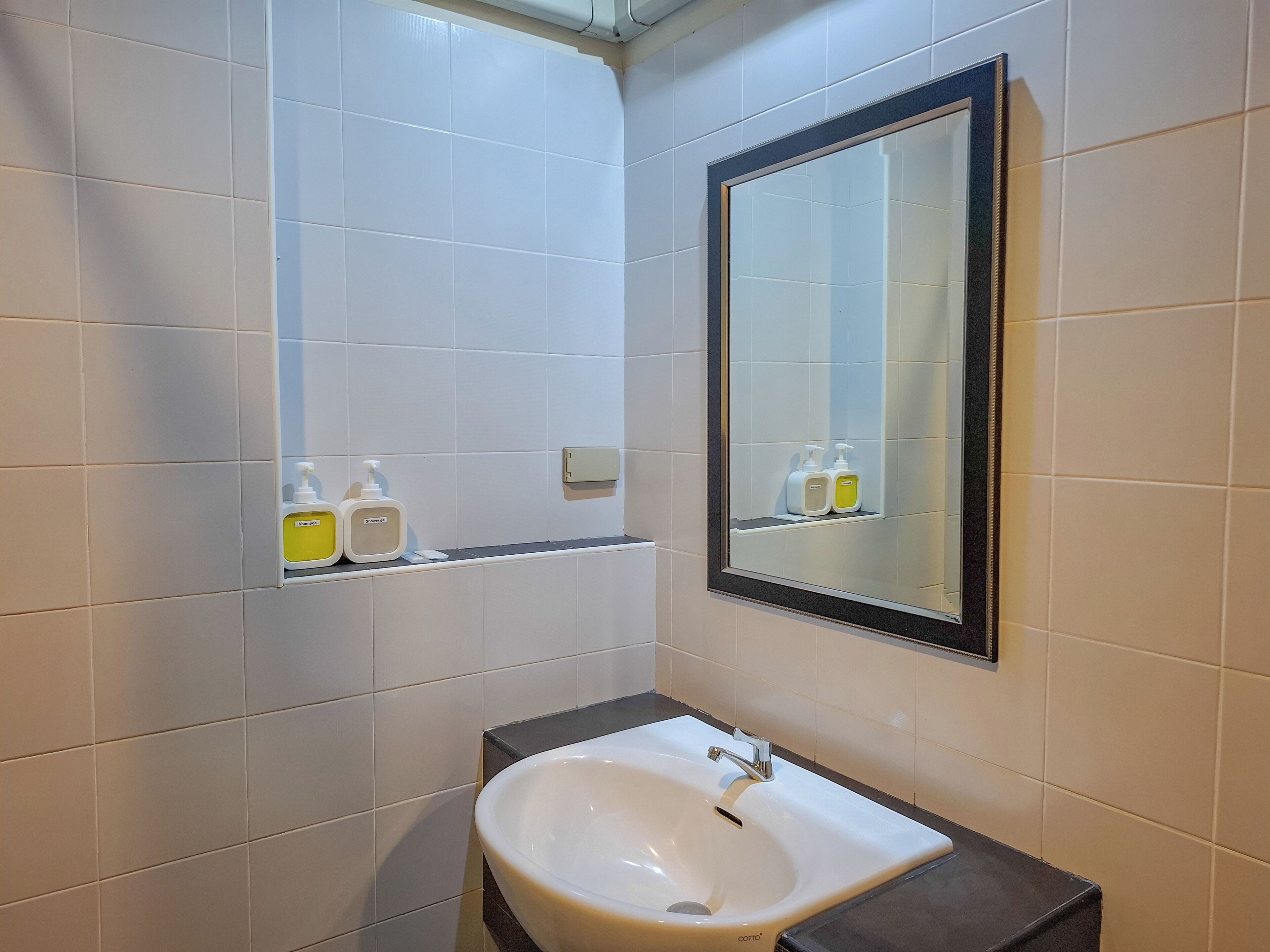 A bathroom with white tiles, a white sink with a single faucet, and a mirror with a black frame.