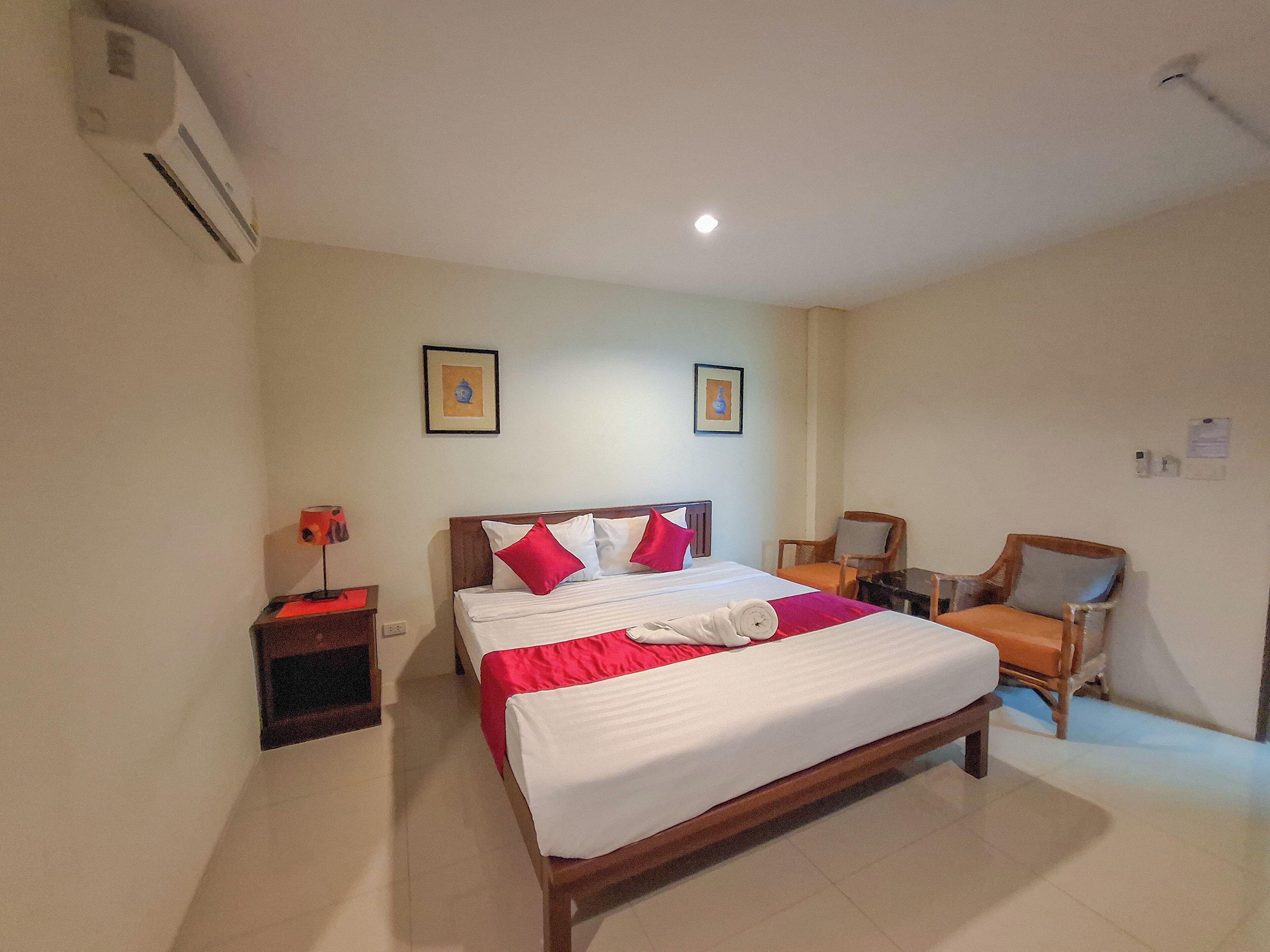 A hotel room with a large bed, two chairs, a nightstand, and a wall-mounted air conditioner.
