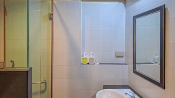 Une salle de bain avec une douche à parois de verre, un lavabo blanc avec un miroir et des articles de toilette rangés sur une étagère.