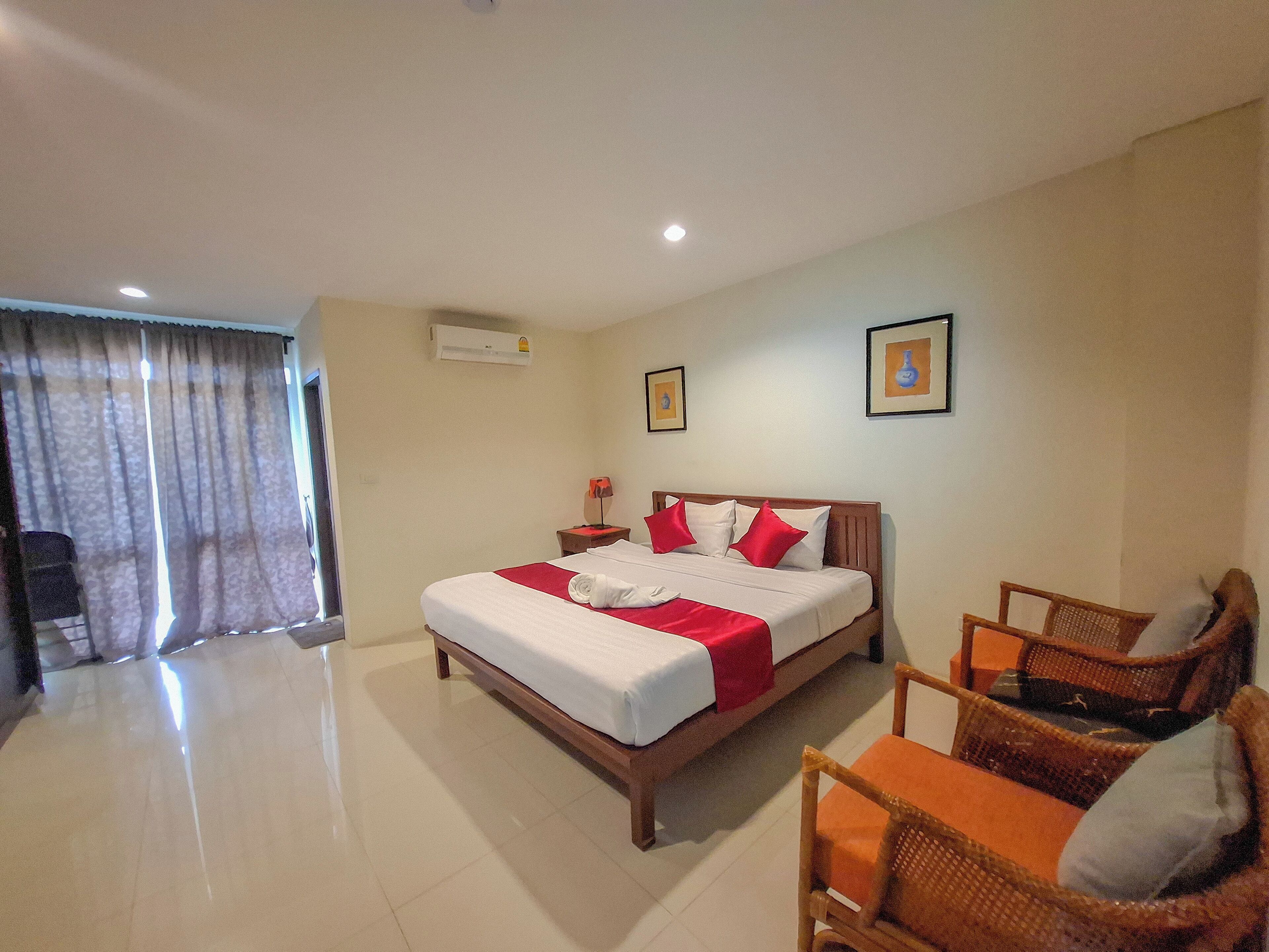A hotel room with a large bed, a chair, a desk, and a window with curtains.