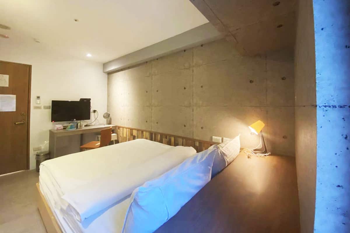 A hotel room with a large bed, a desk with a computer, a television, and a wall-mounted lamp.