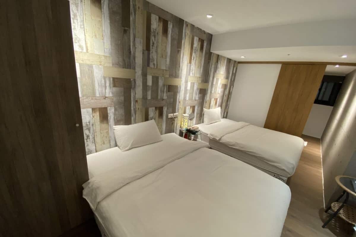 A hotel room with two beds, a wooden accent wall, a small table, and a wooden door.