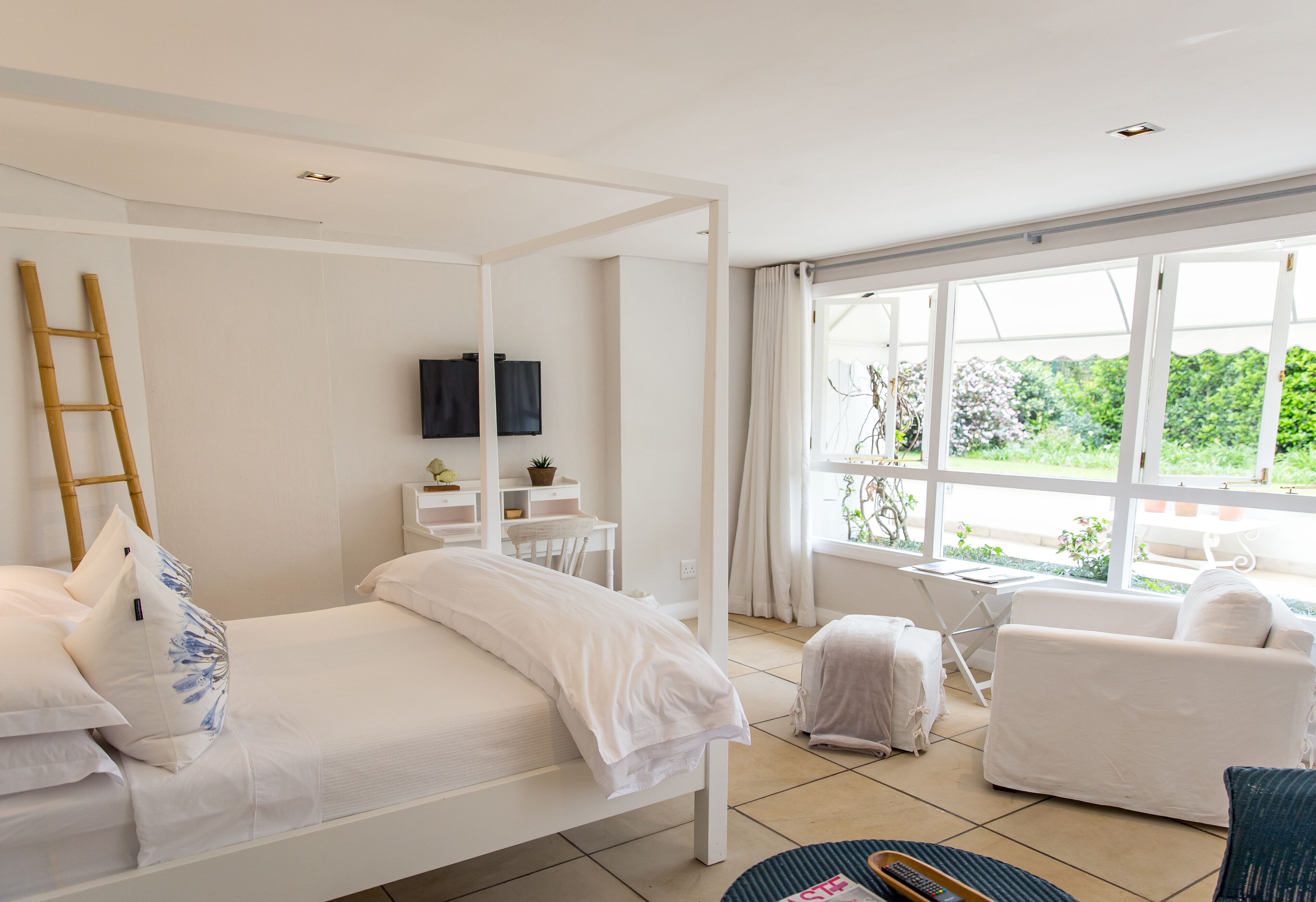 Une chambre à coucher avec un lit à baldaquin, un bureau, une chaise et une vue sur la verdure environnante.