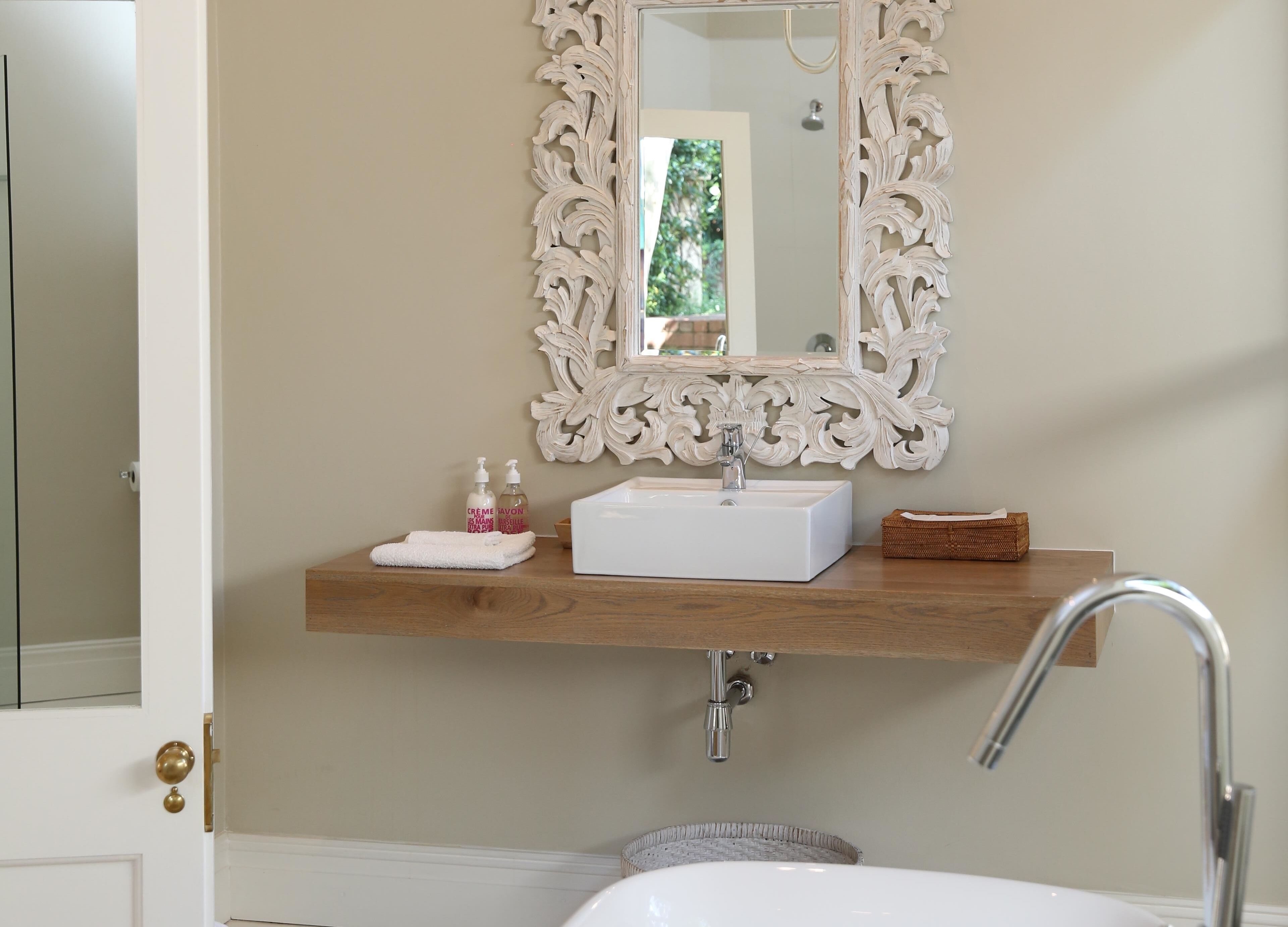 A bathroom with a white sink, a mirror with an ornate frame, and a wooden shelf above the sink.