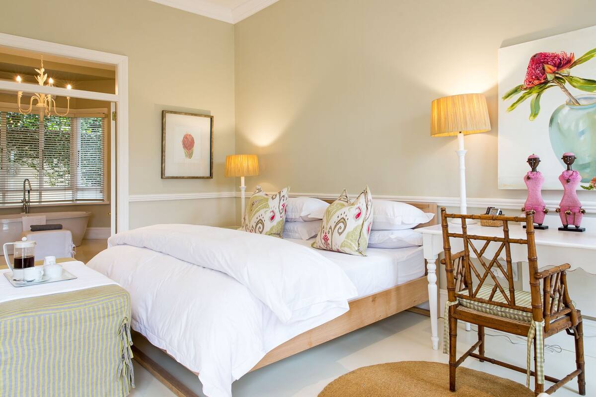 A bedroom with a bed, bedside table, lamp, chair, and artwork.