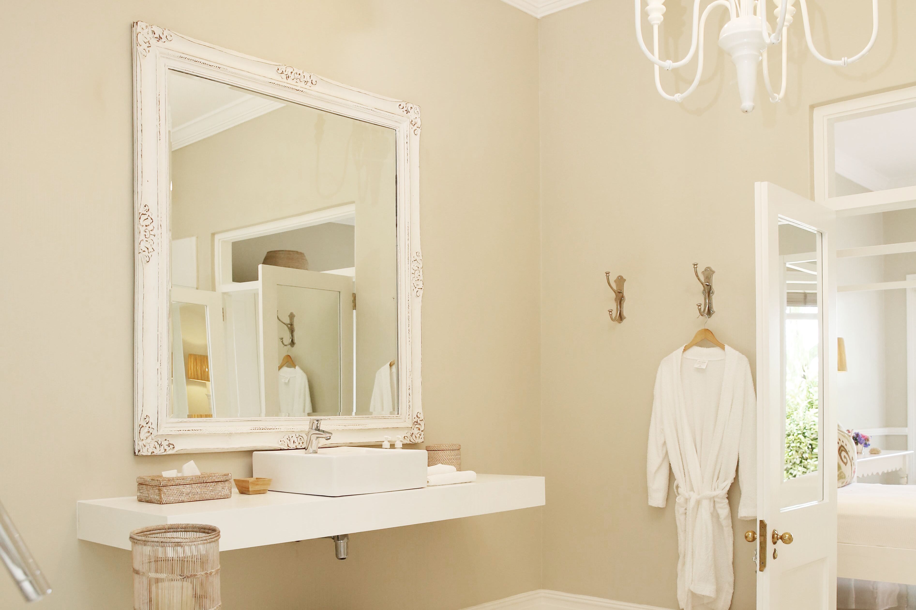 A bathroom with a large ornate mirror, a white vanity, a robe hanging on the door, and a chandelier.