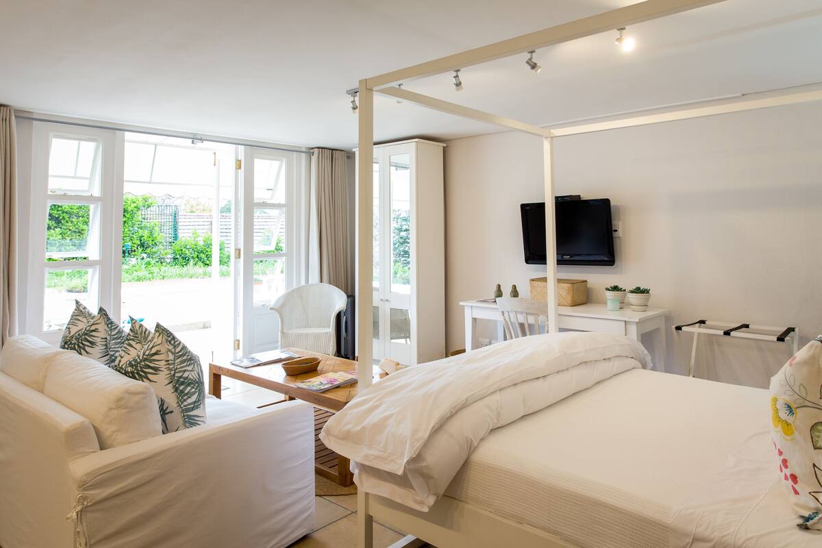A modern bedroom with a four-poster bed, a sofa, a desk, and a television.