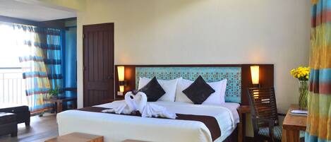 A hotel room with a large bed, a wooden headboard, a small table, a chair, and a view of the outside.
