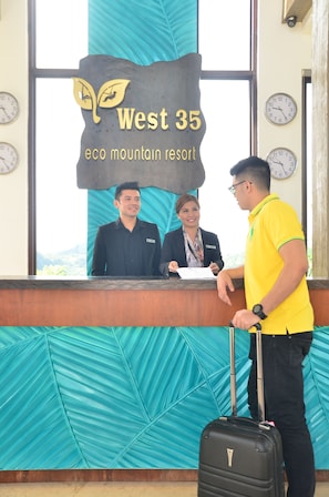 A reception desk at West 35 eco mountain resort with a large sign, clocks on the wall, and a person with a suitcase.