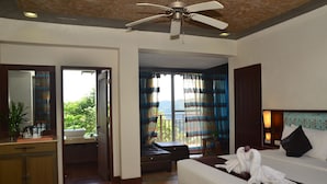 A hotel room with a bed, a desk with a mirror, a bathroom, and a balcony with curtains. - West 35 Eco Mountain Resort (Balamban)