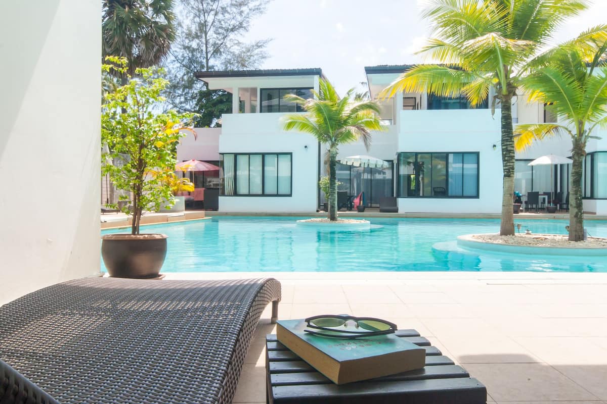 A modern pool area with lounge chairs and a book, surrounded by palm trees and contemporary buildings.