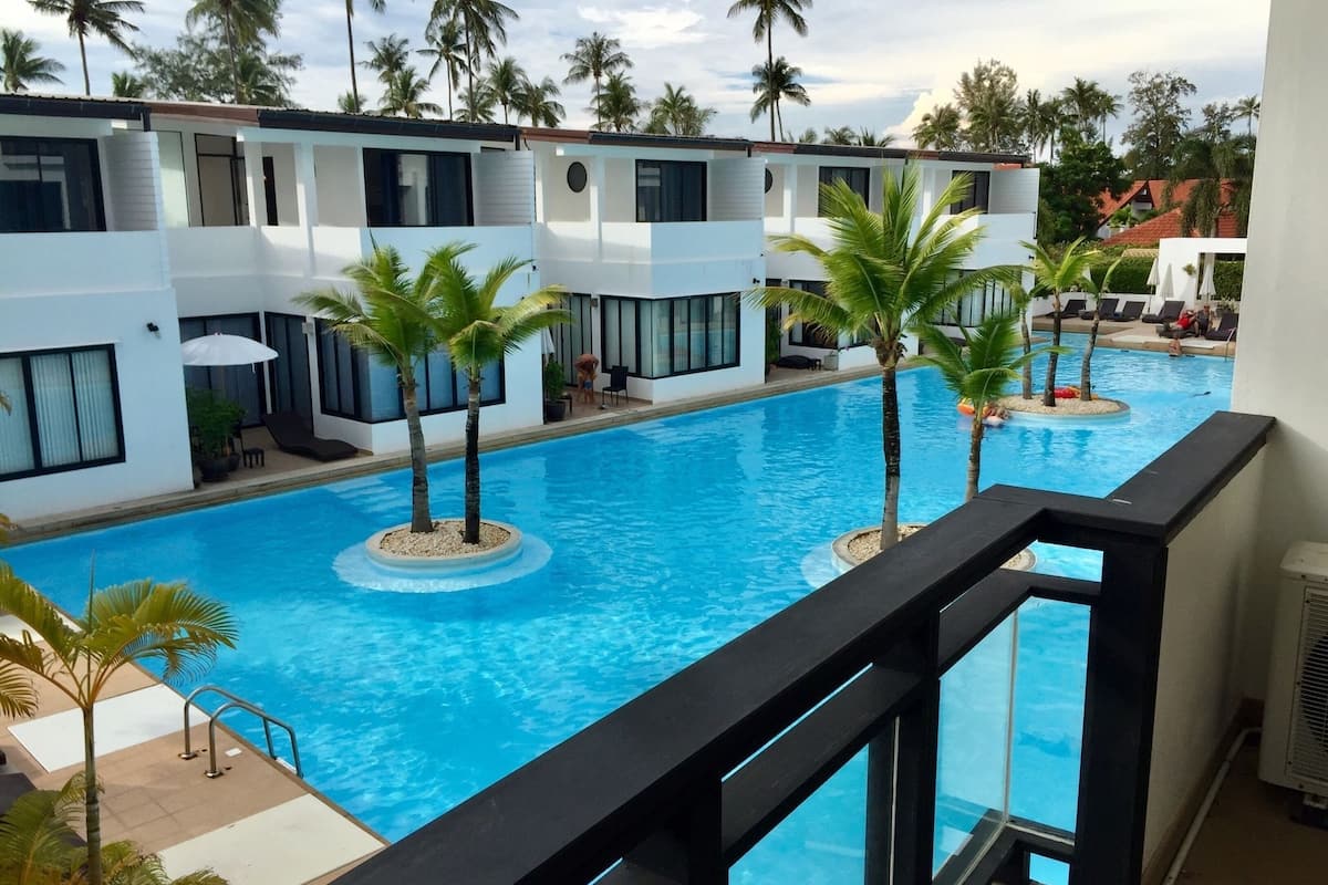 A pool area with a clear view of the pool, palm trees, and a building with multiple windows and balconies.
