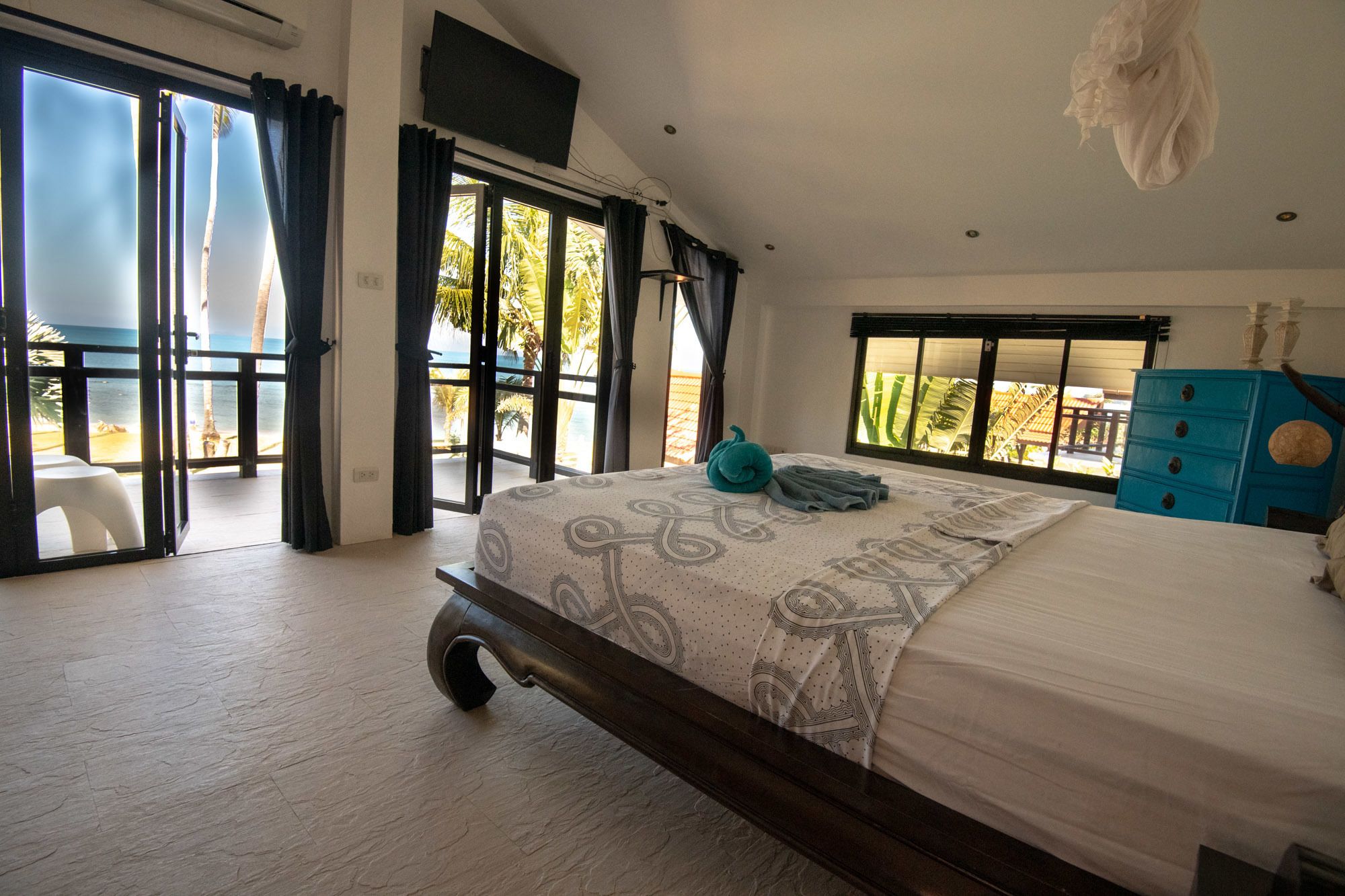 A bedroom with a large bed, a view of the beach, and a balcony with a table and chairs.