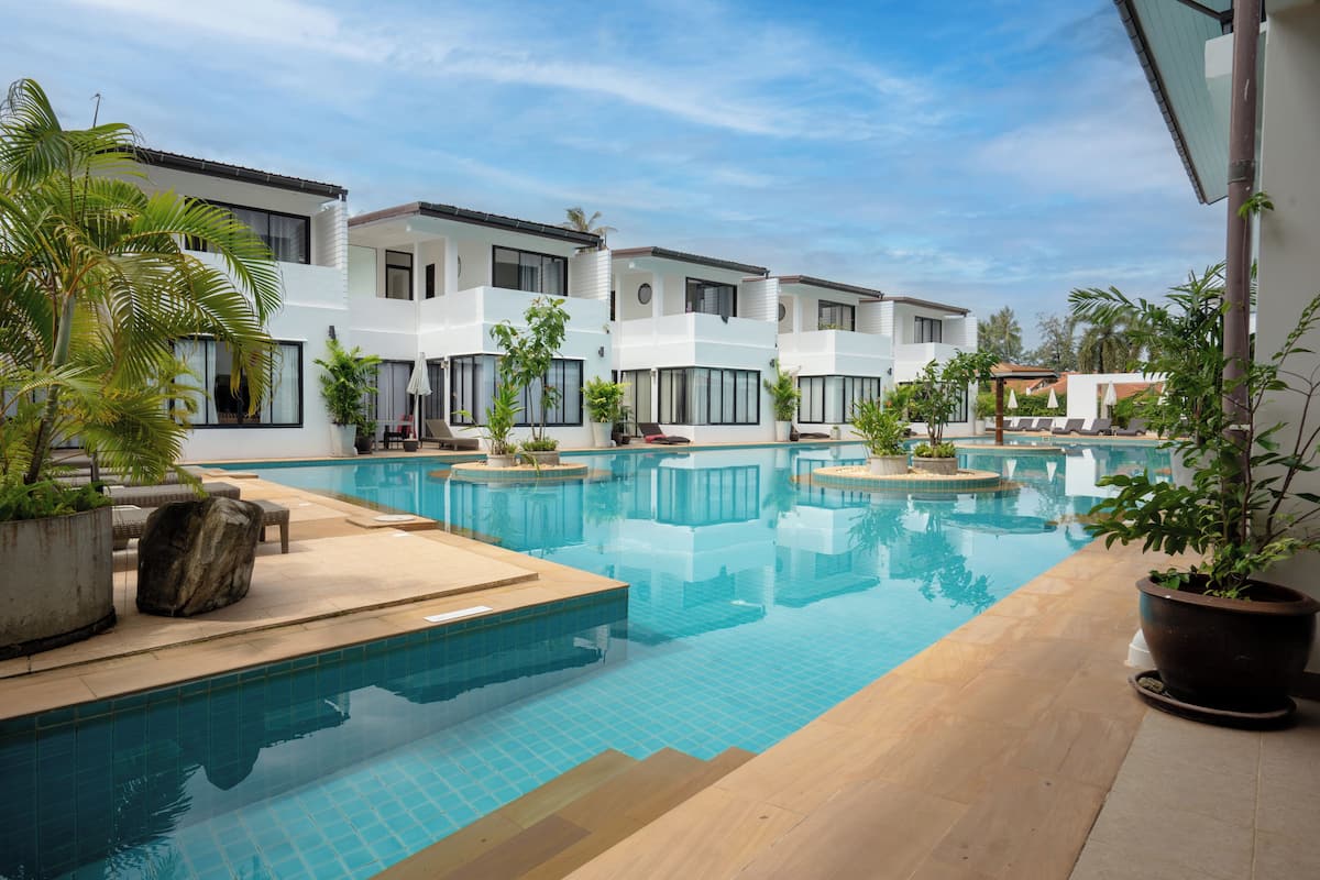 A modern hotel with a swimming pool, potted plants, and a clear blue sky.