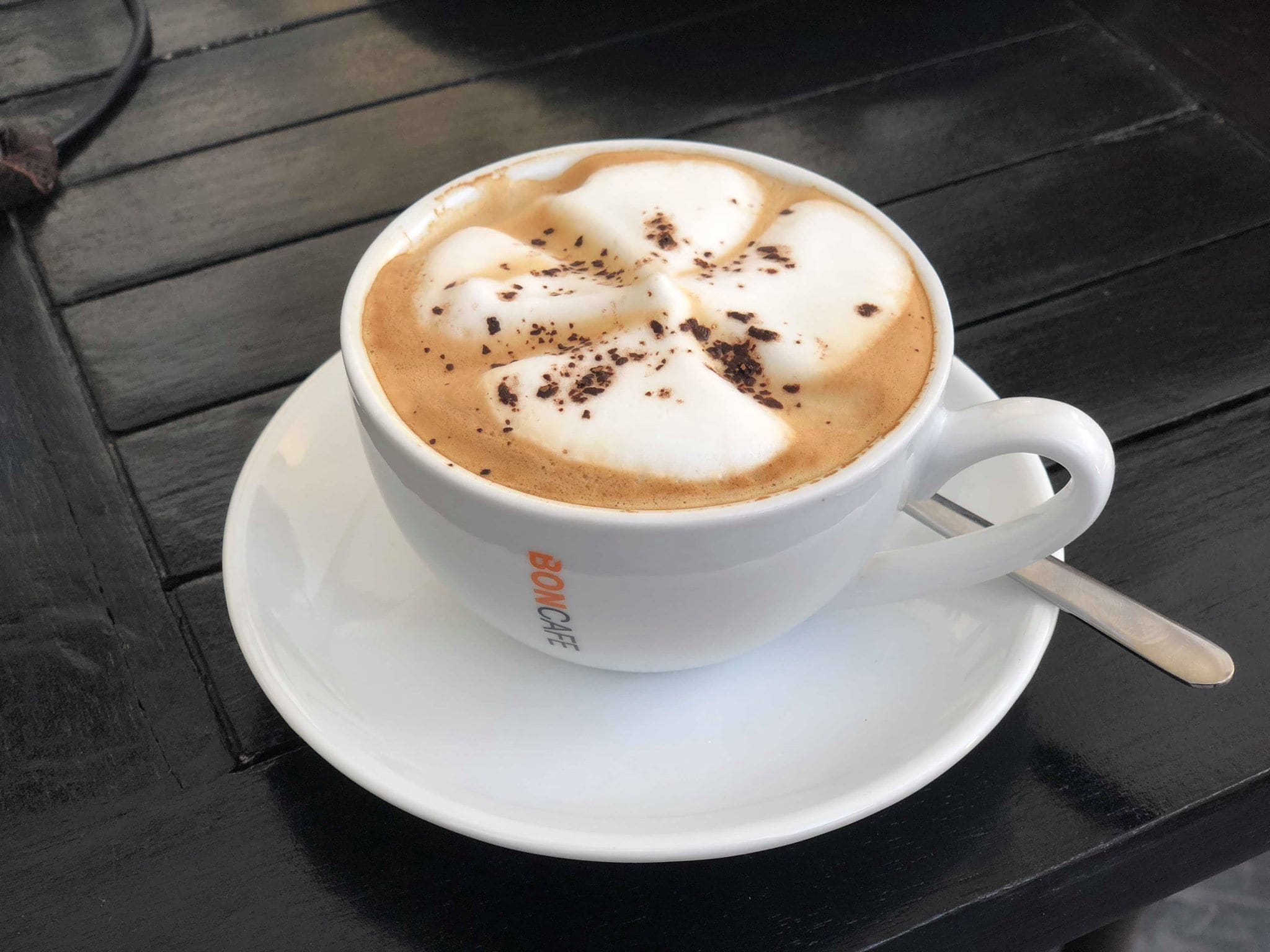 Une tasse de café surmontée d’un motif en latte art, posée sur une soucoupe blanche.