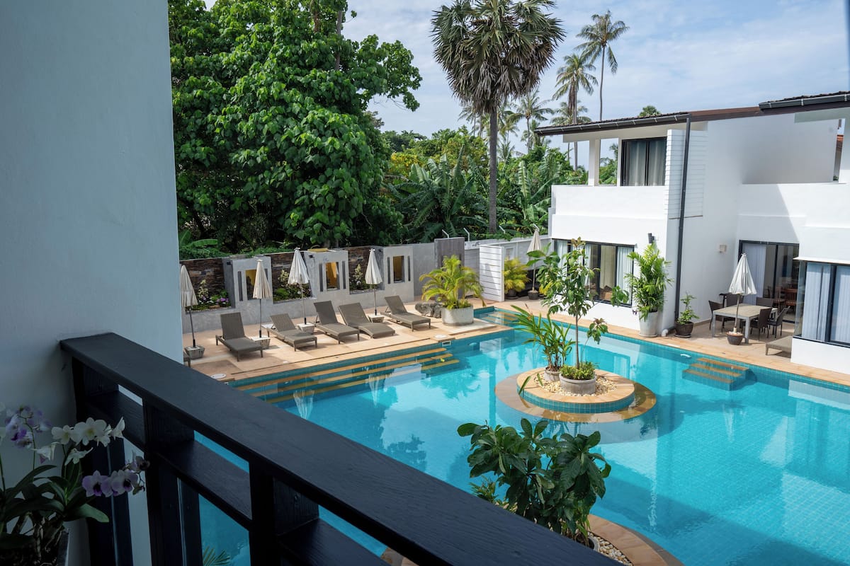 A modern pool area with lounge chairs and umbrellas, surrounded by lush greenery and palm trees.
