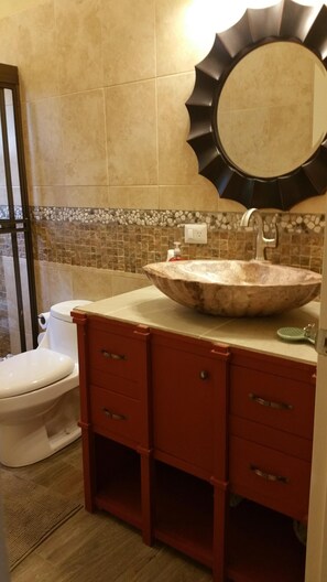 Un baño con un lavabo de piedra, un tocador rojo, un inodoro y un espejo con un marco negro único.