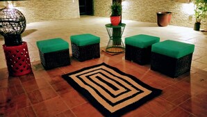 Un hall decorado con alfombra estampada, asientos acolchados verdes, muebles de mimbre y plantas en macetas.