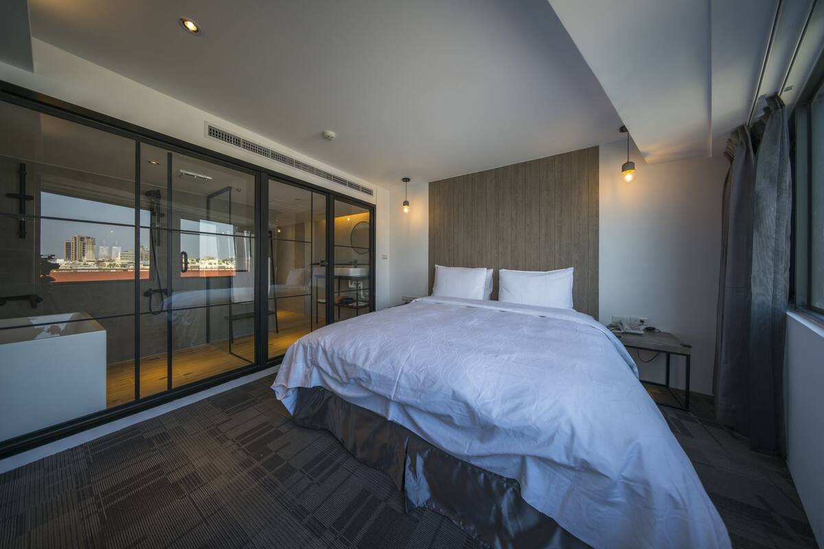 Ein modernes Hotelzimmer mit einem großen Bett, einem Schreibtisch und einer Glasschiebetür, die auf einen Balkon führt.