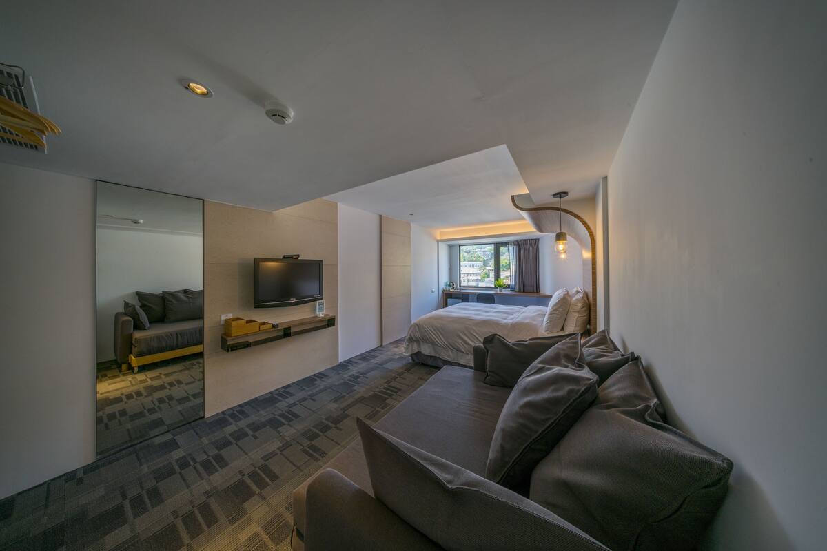 Ein modernes Hotelzimmer mit einem großen Bett, einer Couch, einem Fernseher und einem Spiegel.