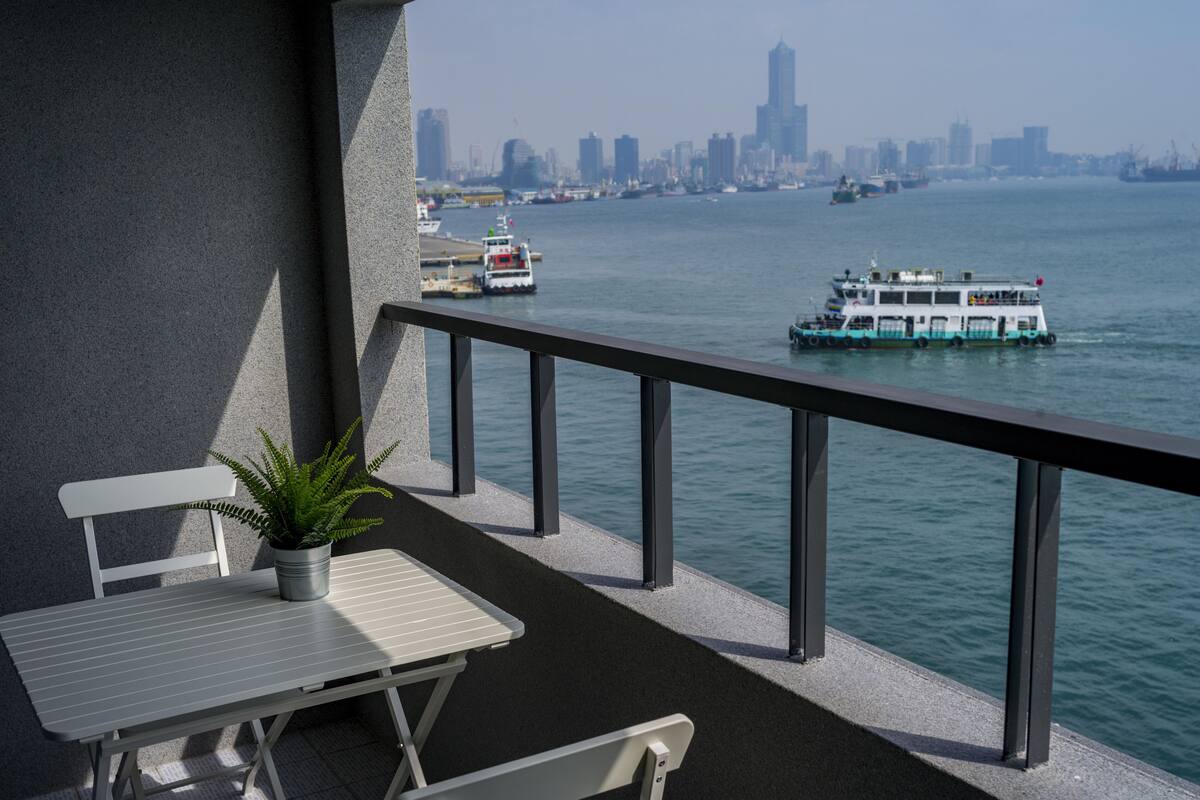 Ein Balkon mit Tisch und Stühlen, der auf ein Gewässer mit Booten und eine entfernte Skyline blickt.
