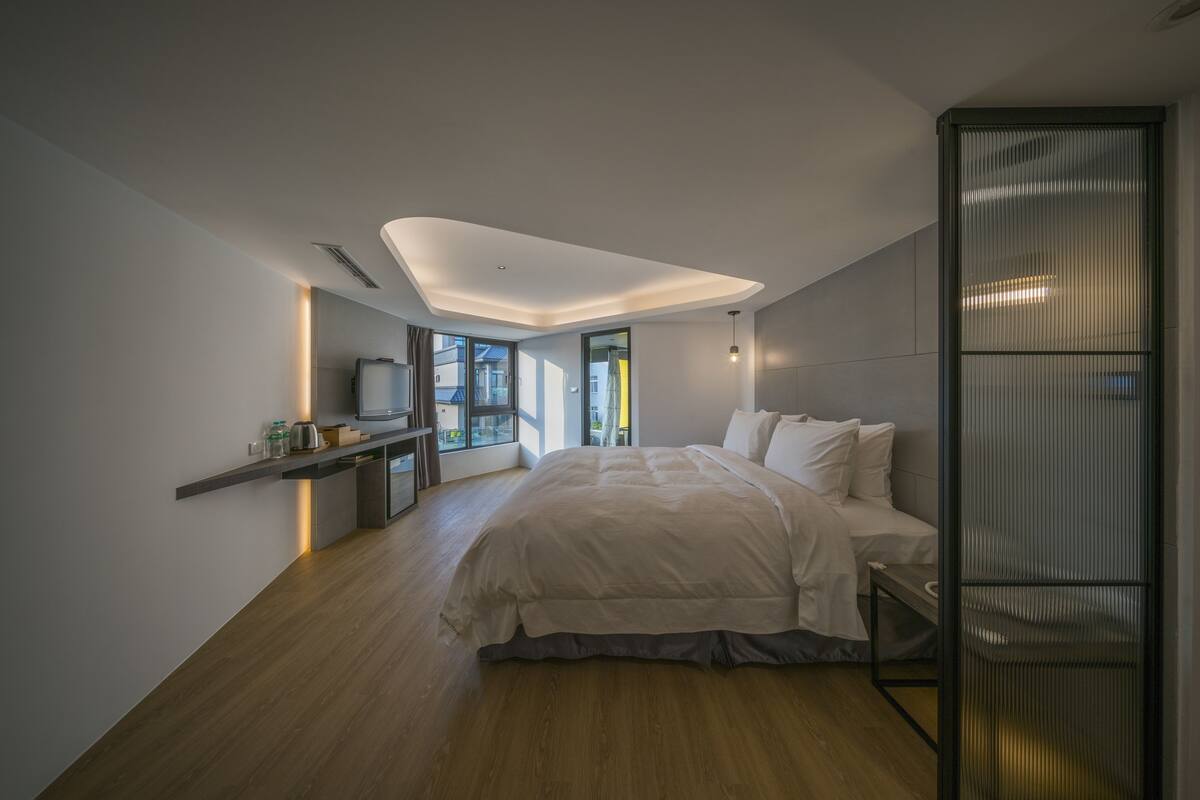 Ein modernes Schlafzimmer mit einem großen Bett, einem Nachttisch, einem integrierten Fernseher und Blick ins Freie.