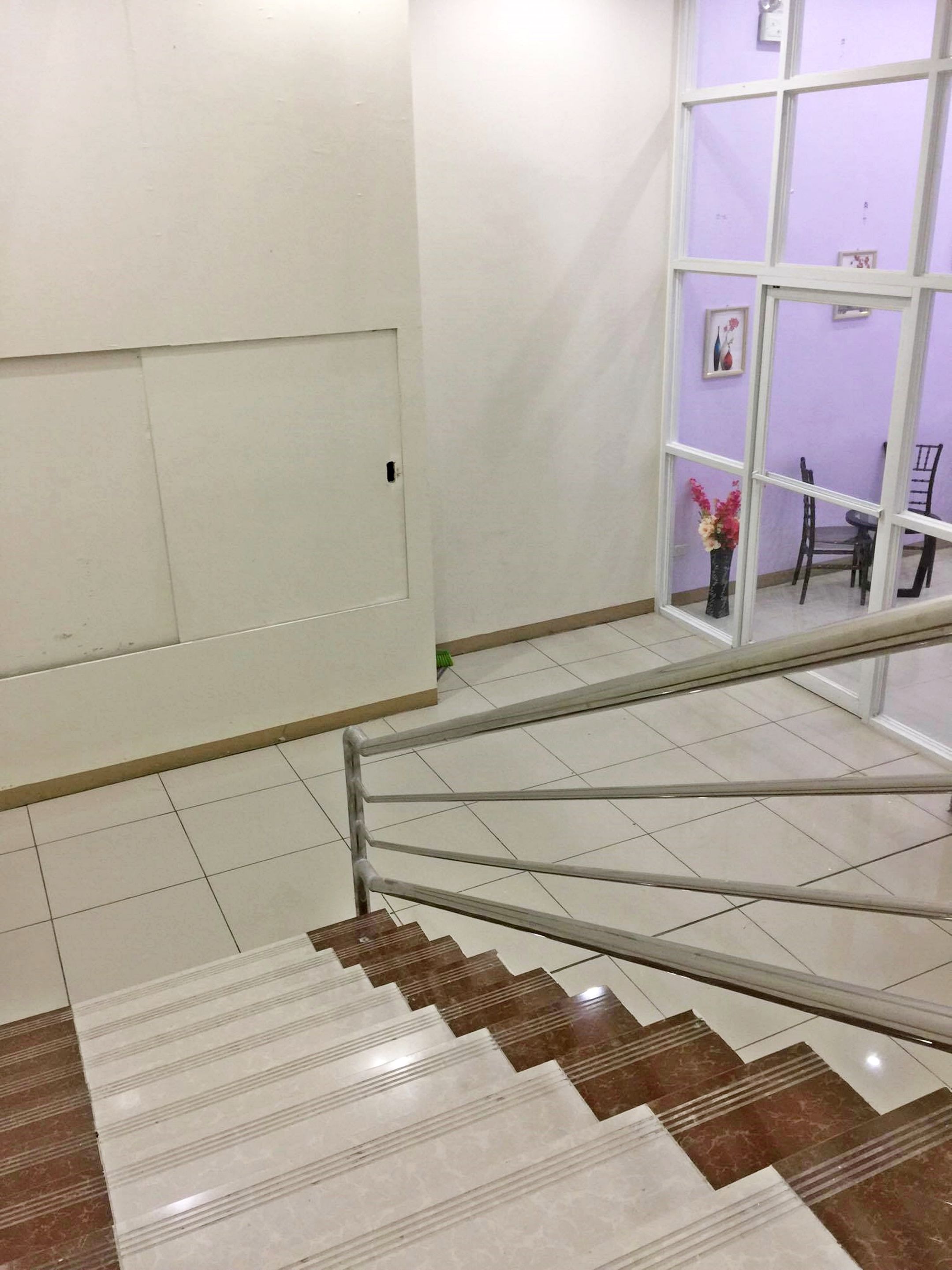 A staircase with a metal handrail, white walls, and a purple wall with a window and a vase of flowers.