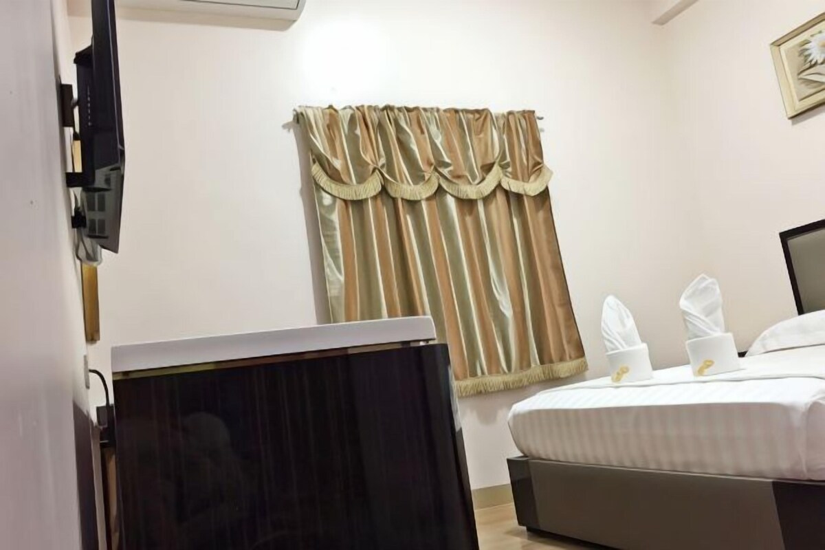 A hotel room with a bed, a TV, and a window with curtains.