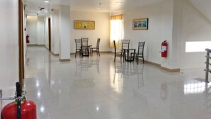 A spacious, well-lit hallway with a dining area featuring a table and chairs, a fire extinguisher, and artwork on the walls. - Meaco Royal Hotel - Lipa (Lipa)