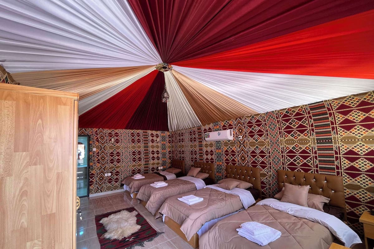 Una habitación con cuatro camas dispuestas en fila, un papel tapiz decorativo y un techo cubierto con tela roja y blanca.