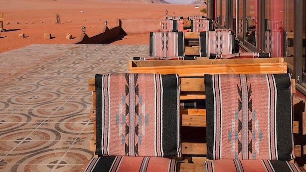 A desert view from a building with a terrace featuring wooden benches and patterned cushions. - Desert Moon Camp (Wadi Rum)
