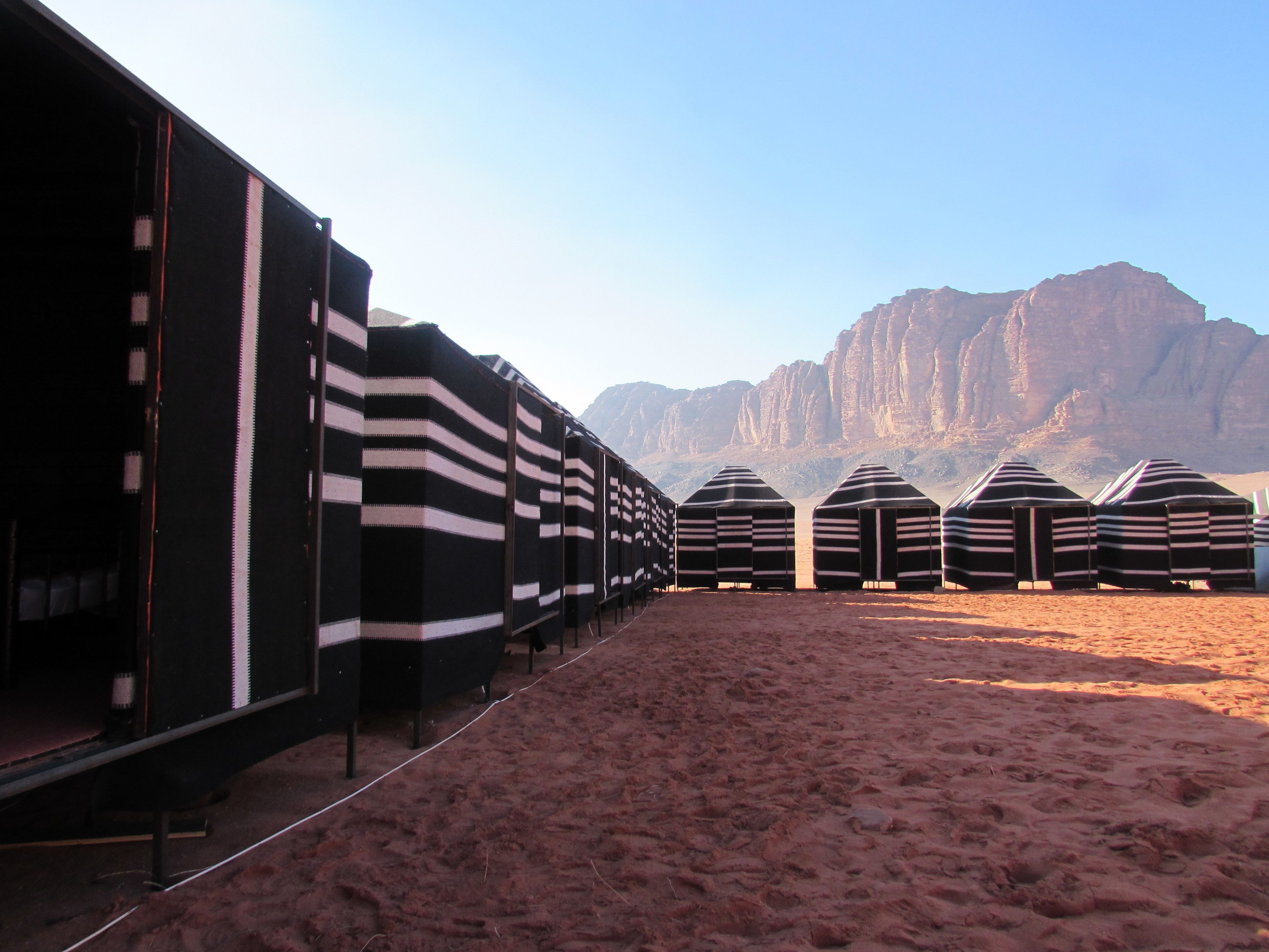 A row of striped tents in a desert setting with a mountain in the background.