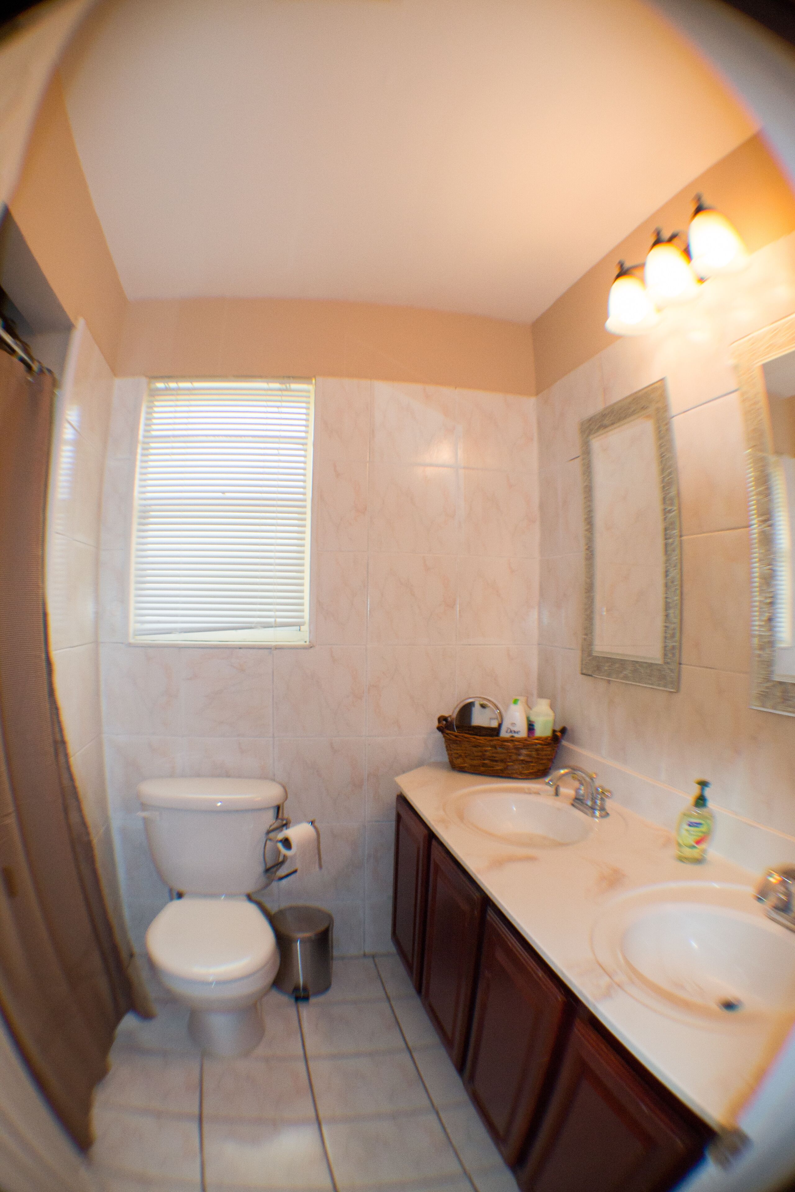 A bathroom with a toilet, two sinks, a mirror, and a window with blinds.