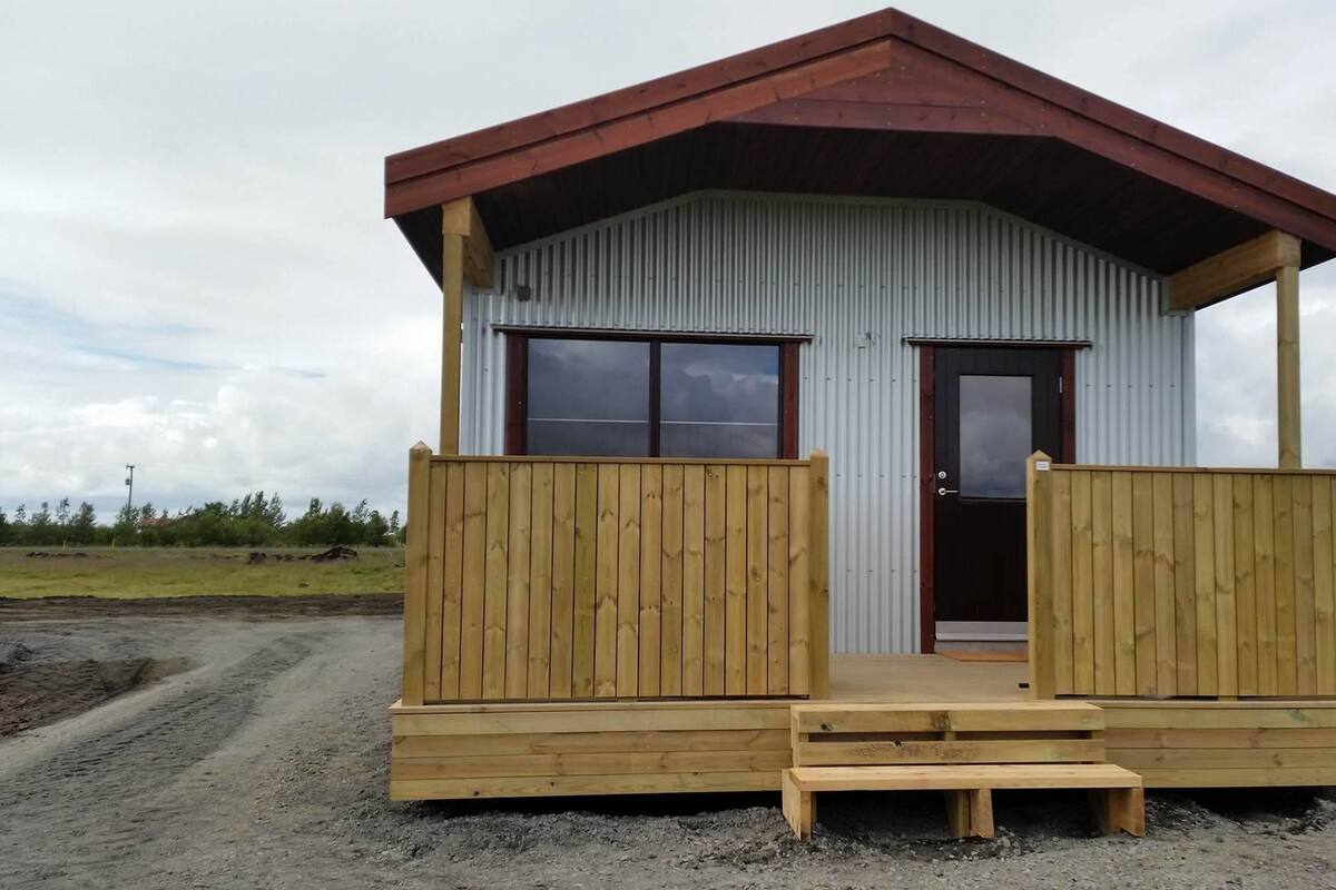 A small wooden cabin with a metal exterior, a dark door, and a wooden porch with steps.