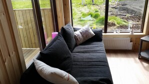 Ein dunkelgraues Sofa mit vielen Kissen, einer rosafarbenen Tasse und einem weißen Heizkörper in der Nähe eines Fensters mit Blick auf einen Garten.