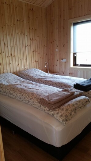 A room with wooden walls, a bed with a patterned duvet, a bedside lamp, and a window with a view. - Hekla Cabin 1 Volcano and Glacier View (Rangárþing ytra)