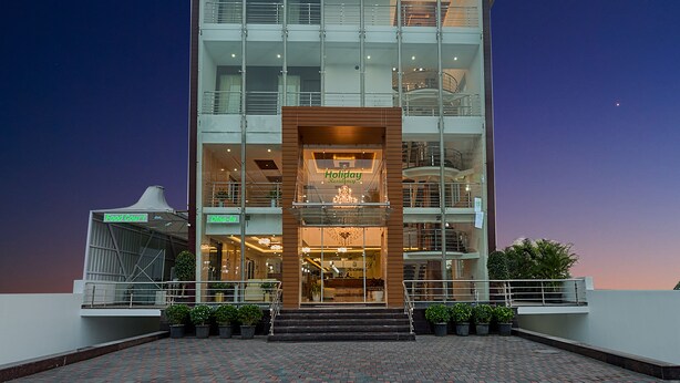Un hotel de varios pisos con fachada de vidrio, un cartel que dice "Holiday Residence" y una escalera que conduce a la entrada.
